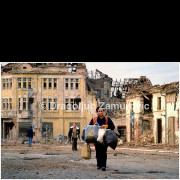 Vukovar (Croatia) – November 18, 1991

A woman walks through the devastated streets of Vukovar, carrying her remaining belongings, on the day the city fell after months of siege and destruction.
Behind her, ruined buildings and collapsed roofs bear witness to the intensity of the fighting and the scale of civilian suffering.

The photograph records an ordinary human gesture — carrying what is left — set against the extraordinary devastation of a city almost entirely destroyed. It stands as a quiet testimony to the civilian experience of war, displacement, and survival.