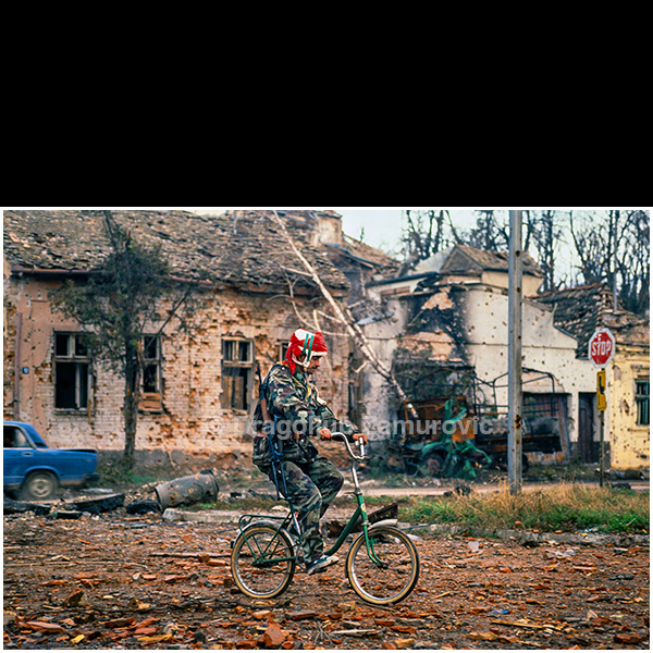 Amid the total destruction of Vukovar, surreal scenes appeared everywhere throughout the city. One of them shows a soldier riding a bicycle through streets covered with rubble and debris, surrounded by ruined houses marked by shelling and fire.
In a landscape stripped of normal life, such moments revealed the absurd contrast between everyday objects and the reality of war. The photograph records this quiet, almost unreal fragment of daily movement inside a city that had ceased to function as a city.
