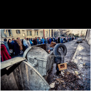 The introduction of international sanctions against the Federal Republic of Yugoslavia in 1992 triggered a severe economic crisis, hyperinflation, shortages of basic goods, and a dramatic decline in living standards. Ordinary citizens bore the heaviest burden of these measures.

The photograph shows a scene from Belgrade: a long line of people waiting patiently, while in the foreground a man searches through garbage containers for usable items. Such scenes became a daily reality during the 1990s, serving as powerful testimony to social collapse, poverty, and the struggle for basic survival.