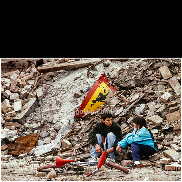 Six months after the Yugoslav People’s Army entered Vukovar, I returned to document the city after the fighting had ended. There were no tanks, no gunfire, no burning buildings anymore, yet the silence that filled the streets was overwhelming. Ruins were everywhere, and only an occasional house showed signs of reconstruction.
In this devastated environment, I encountered two children sitting beside a pile of rubble marked by a damaged school traffic sign. Their bicycles lie abandoned in front of them. The scene quietly reveals how childhood continued amid destruction, surrounded by symbols of a normal life that had abruptly disappeared.