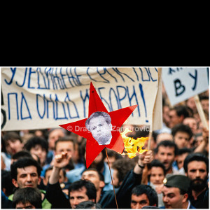 A protest against Slobodan Milošević in Belgrade in 1990, where demonstrators burn a red five-pointed star bearing his portrait, transforming a historic symbol into a sign of public revolt against authoritarian rule.