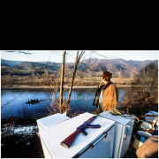 In January 1993, during the war in Bosnia and Herzegovina, large numbers of refugees crossed the Drina River from Bosnia into Serbia. Reports of this mass movement brought me to the riverbank near the village of Crvice, where I encountered scenes that exceeded any prior expectations.
People were leaving their homes carrying only basic belongings, crossing the river in improvised boats, often in harsh winter conditions. Among the refugees were men, women, and elderly people. One striking detail was the presence of firearms — not hunting rifles, but military weapons — carried by some of those fleeing.
This photograph captures a moment on the riverbank: improvised luggage, a rifle placed on household appliances, and a man looking toward the river as a boat with refugees reaches the opposite shore. The image stands as a documentary record of one of many, rarely documented episodes of wartime displacement during the winter of 1993.